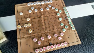 Unlike the previous two three-player variants of Chinese Chess/象棋/Xiangqi, this version is fully professional (and has a decently long history).  The board is professionally printed, the pieces custom made for the set, and the rules, instead of being a bunch of JPG images (first game) or little strips of paper that look like they were printed on a POS terminal (second game), are printed professionally on proper print stock with colour ink.

Of course you pay for what you get.

This game has almost no changes to piece movement, but as with the first game lacks the key strategy of pinning opposition.  It also has four sides, despite there being only three players.  The yellow pieces to the left are the fourth side and they begin the game aloof.  They do nothing (and can have nothing done to them) until a piece of any of the other teams reaches the black spots around the yellow general.  The specific spot landed on determines who is now allied with the yellow pieces--whoever that is adds the yellow pieces to their own forces--while the other two team up to fight against them.

The yellow pieces are VERY powerful (three chariots and a cannon), so don't let the low piece count fool you.

As with the first game, it's hard to use cannon pins.  As with the second game, the middle part adds a dimension to the board, in this case a sizable dimension (9x9 grid) which changes some key movement and placement strategies.